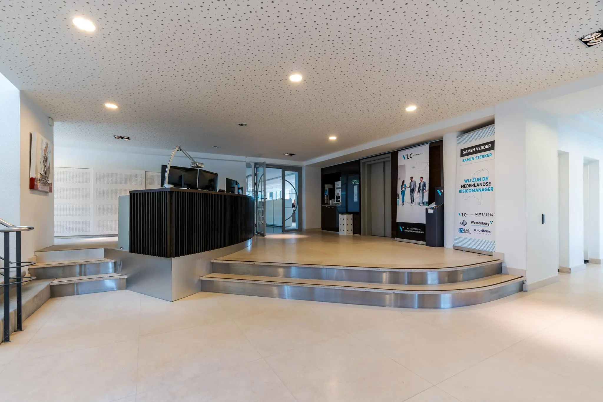 Moderne entreehal met ontvangstbalie en posters van VLC & Partners aan de Van Alkemadelaan.